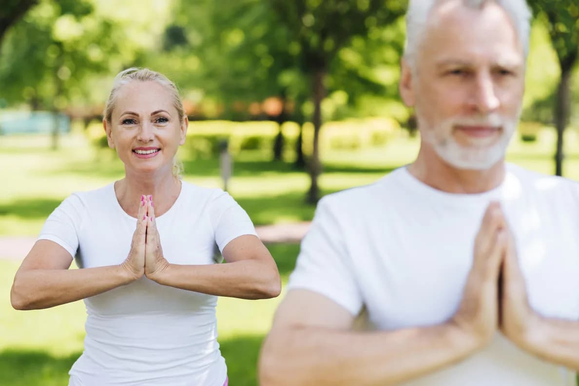 Parkta, elleri göğüs hizasında birleşmiş yoga yapan orta yaşlı bir çift